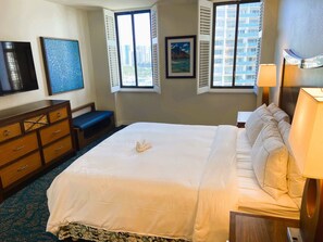 A hotel room with a large bed, a desk, a chair, a TV, and a window with a city view. - Hilton Hawaiian Village Lagoon Tower Oceanfront Premier 2-Bed, 2-Ba Condo (Honolulu)