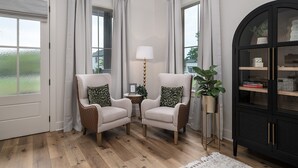 A room with two armchairs, a lamp, a cabinet, and a view of greenery outside. - The  Willow  Cottage (TYLER)