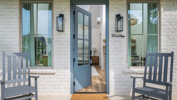 A building entrance with a blue door, two grey rocking chairs, and a white brick wall. - The  Willow  Cottage (TYLER)