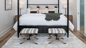 A four-poster bed with a white and black color scheme, two bedside tables with lamps, a white shaggy rug, and a circular light fixture above the bed. - The  Willow  Cottage (TYLER)