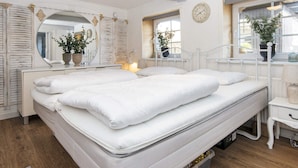 A bedroom with a large bed, a bedside table, a mirror, and two windows with plants. - 4 Person Holiday Home in Skaerbaek (Skaerbaek)