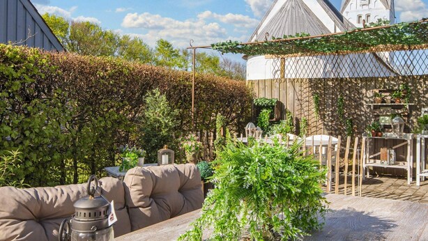 A cozy outdoor seating area with a wooden table, cushioned chairs, and lanterns. - 4 Person Holiday Home in Skaerbaek (Skaerbaek)
