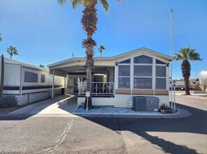 A small, single-story building with a flat roof, a covered entrance, and a small porch area. - Cozy Bright Park Model, Vibrant 55+ many Amenities (Mesa)