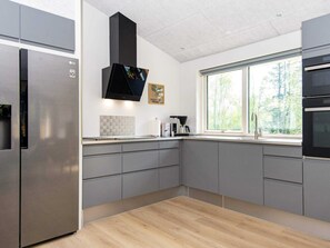 A modern kitchen with a stainless steel refrigerator, a black range hood, and a window with a view of trees.