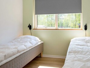 A bedroom with two single beds, a window with a view of trees, and a wall-mounted lamp.