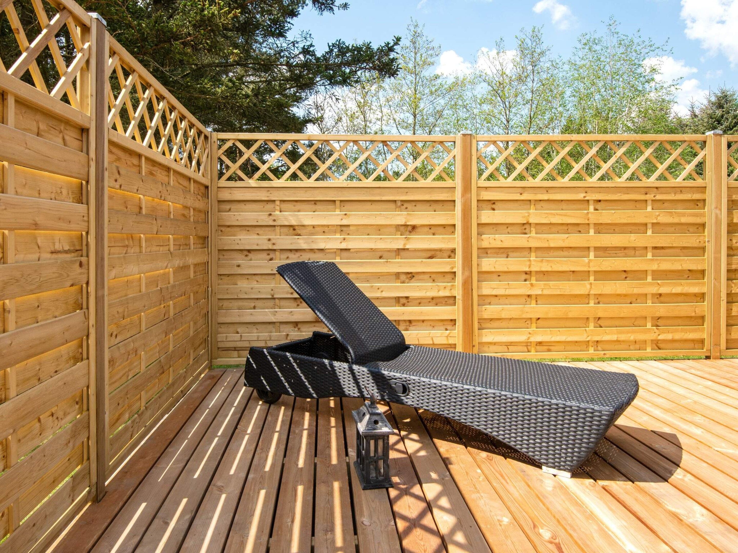 A wooden deck with a metal-framed lounge chair and a lantern.