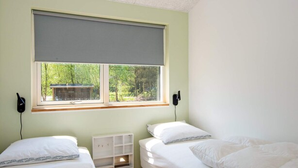 Ein Zimmer mit zwei Betten, einem Fenster mit Blick ins Grüne, einer Schrankwand und einer Wandleuchte.