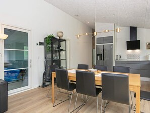 Une cuisine moderne dotée d’un réfrigérateur encastré, d’une table à manger avec des chaises et d’un meuble vitré contenant des plantes.