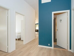 A hallway with a blue accent wall, a white door with a toilet symbol, and a bed in the background.