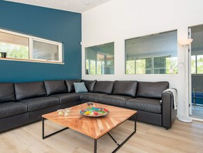 A modern living room with a black leather sofa, a wooden coffee table, and large windows. - 4 Star Holiday Home in Oksbol (Oksbol)