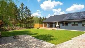 Ein modernes Haus mit überdachter Terrasse, Solaranlage und gepflegtem Rasen.