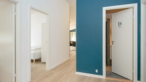 Ein Flur mit einer blauen Akzentwand, einer weißen Tür mit einem Toilettensymbol und einem Bett im Hintergrund.