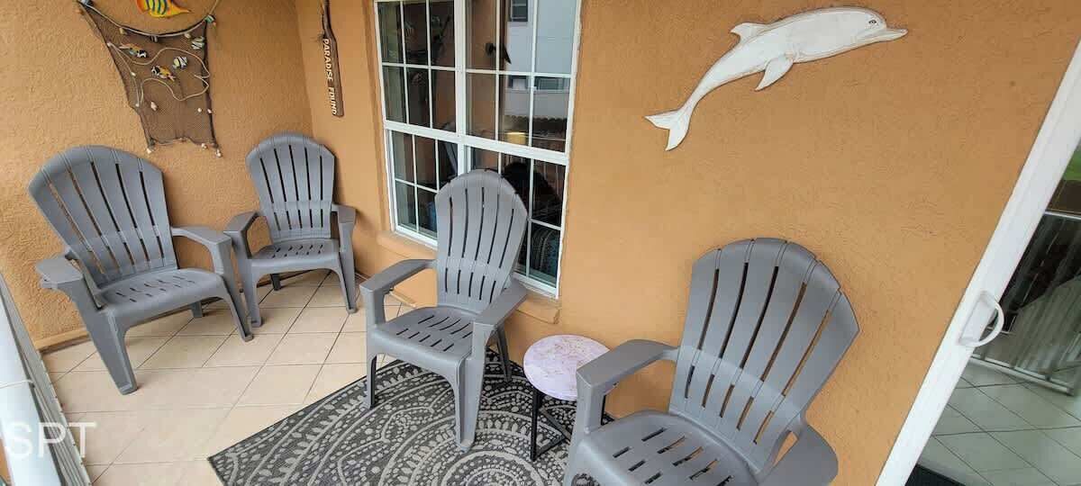 A patio area with four grey plastic chairs, a small round table, and a decorative wall piece of a dolphin.
