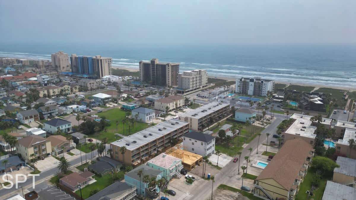 An aerial view of a coastal town with buildings, a beach, and a parking lot.