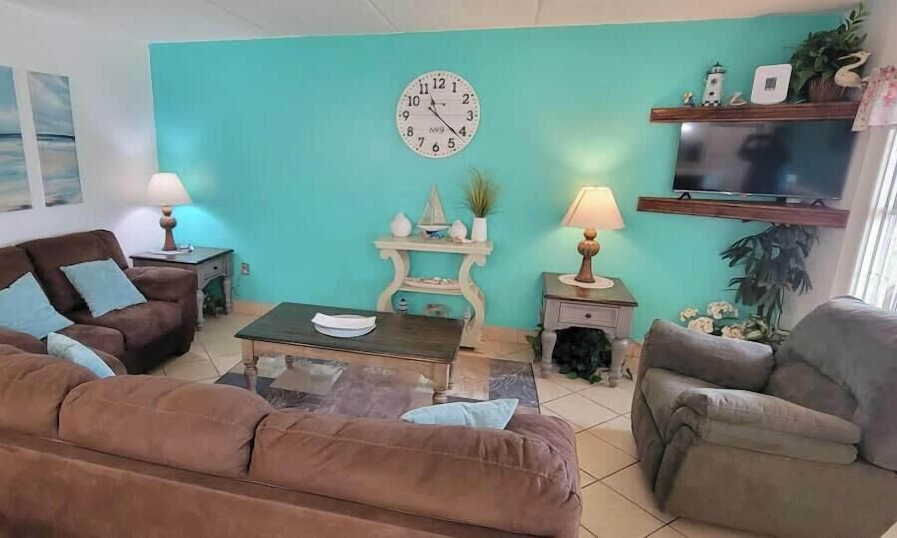A living room with a teal wall, a round clock, a television, and a coffee table.