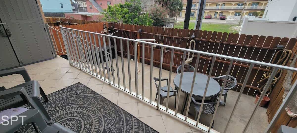 Un balcon avec une balustrade en métal, une table ronde avec des chaises et un tapis à motifs.