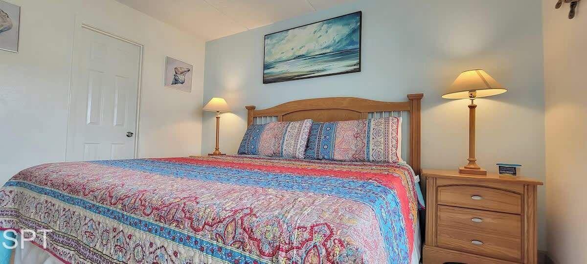 A bedroom with a large bed, two bedside tables, a wooden headboard, and a painting on the wall.
