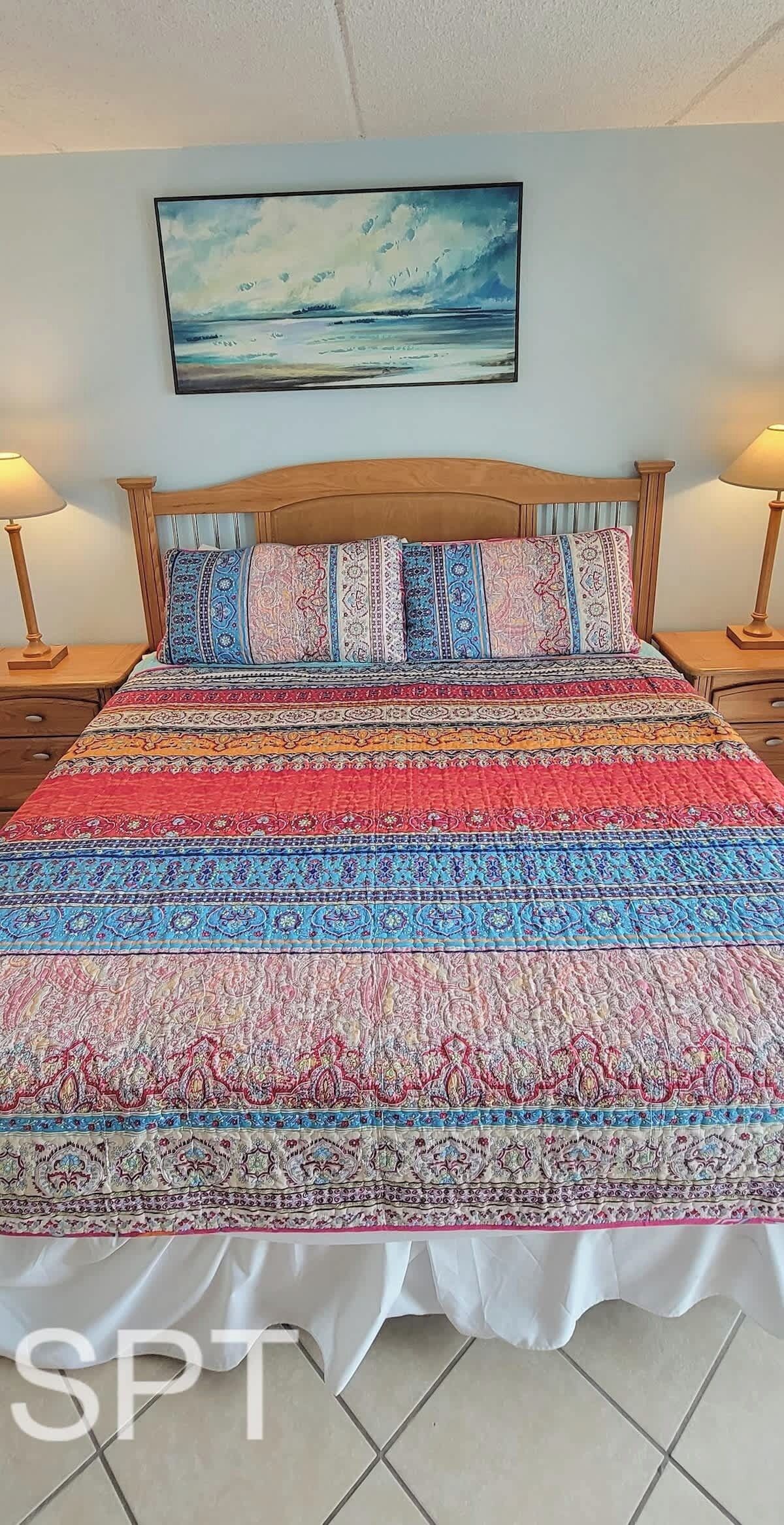 Una cama con un colcha de colores, un cabecero de madera y un cuadro encima.