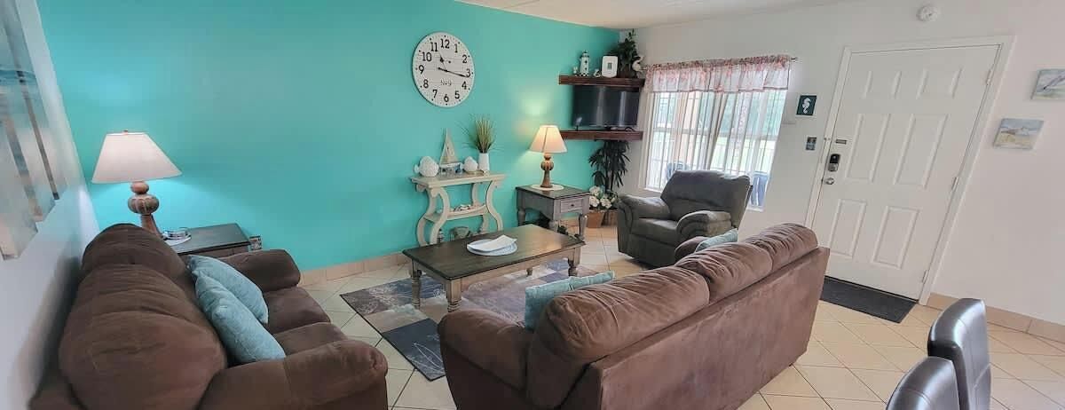 A living room with a teal wall, a brown sofa, a coffee table, a TV, and a door.