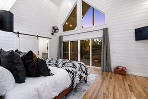A bedroom with a bed, pillows, a large window, and a sliding glass door leading to an outdoor area.
