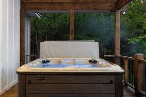 A hot tub with two jets, a control panel, and a brand label on a wooden deck with a view of trees.