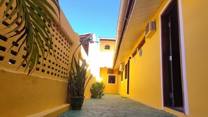 A narrow alleyway with yellow walls, a potted plant, and a door on the right. - Pousada Caminho das Estrelas (Mata de São João)