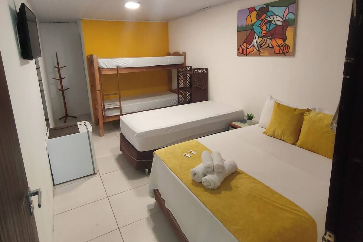 Ein Zimmer mit einem Etagenbett, einem Einzelbett mit gelber Bettwäsche, einem kleinen Schreibtisch und einem Bild an der Wand.