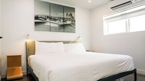 A modern bedroom with a bed, a wall-mounted air conditioner, a window, and a multi-panel artwork above the bed. - The Escape - Suite 4 (Venice)
