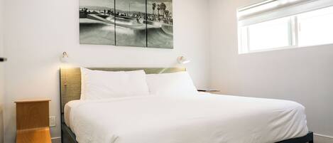 Een moderne slaapkamer met een bed, een wandairconditioner, een raam en een meerdelig kunstwerk boven het bed.