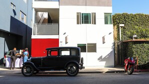 A vintage black car parked on a street, a red and white building, and a motorcycle. - The Escape - Suite 4 (Venice)