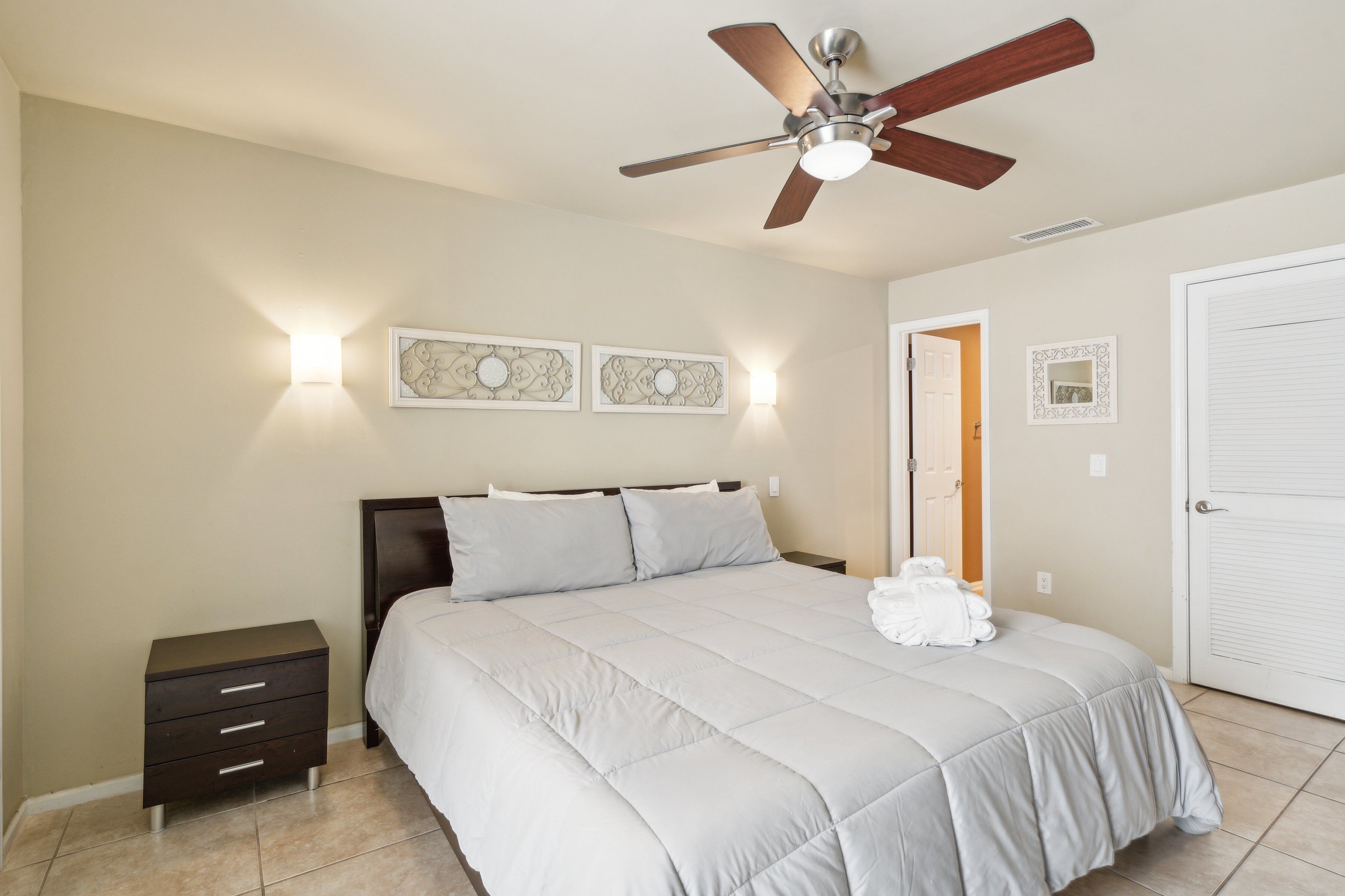 A bedroom with a bed, a nightstand, a ceiling fan, and wall-mounted light fixtures.