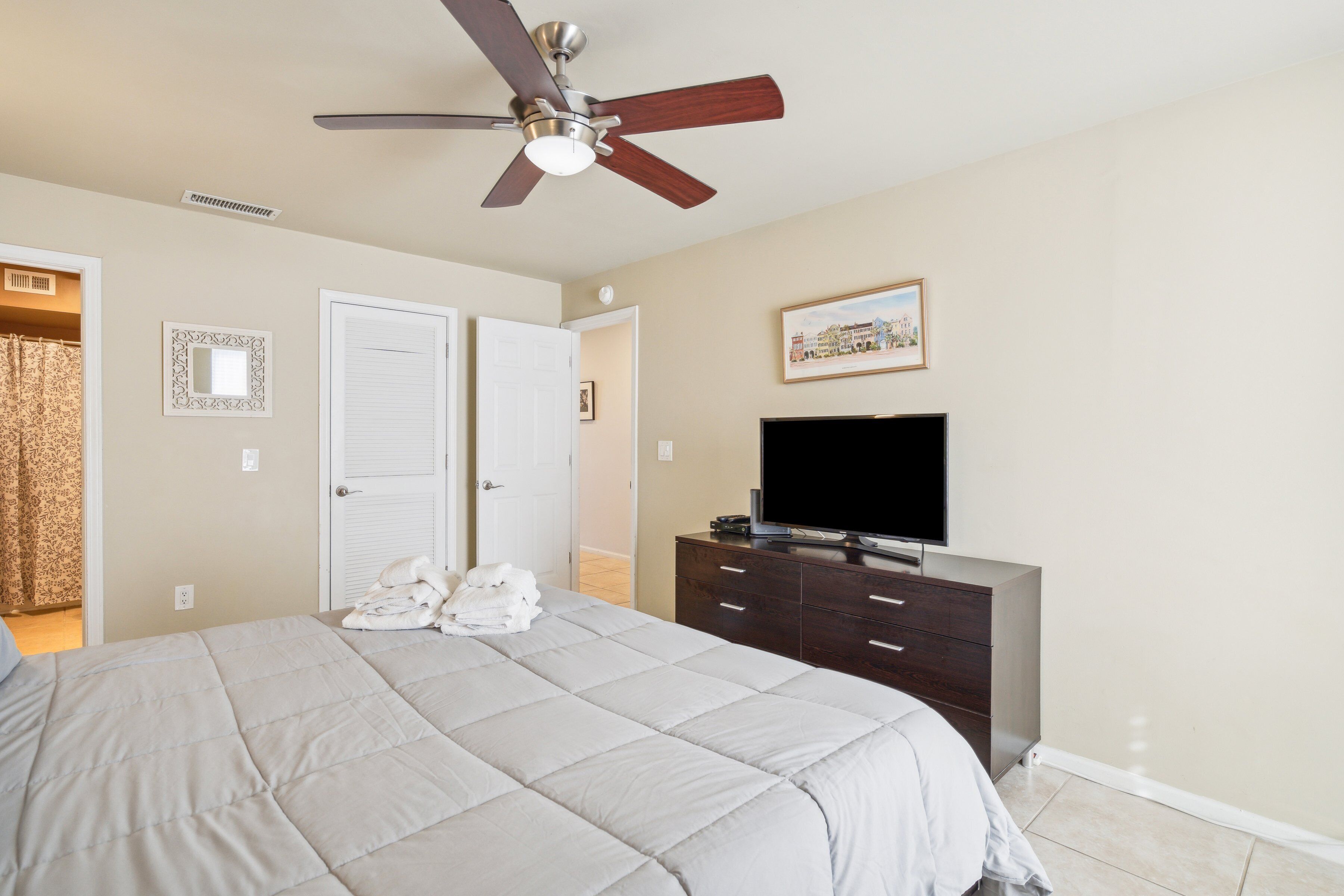 A bedroom with a bed, a ceiling fan, a dresser, a TV, and a door.