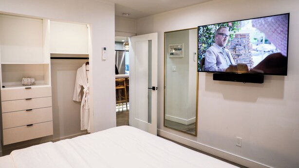 Une chambre à coucher comprenant un lit, une armoire, un téléviseur fixé au mur et une porte-fenêtre coulissante donnant sur une salle de bain.