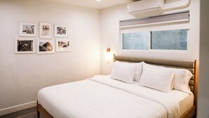 Une chambre à coucher avec un lit, un climatiseur fixé au mur, une fenêtre et plusieurs tableaux encadrés accrochés au mur.