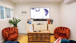 Un salon comprenant un téléviseur, deux fauteuils, une table basse en bois et une plante.