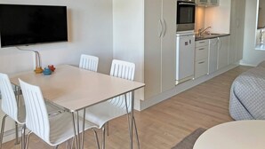 Moderni keittiö, jossa on valkoiset kaapit, mikroaaltouuni ja pesuallas. Keittiössä on myös ruokailutila, jossa on pöytä ja tuolit.