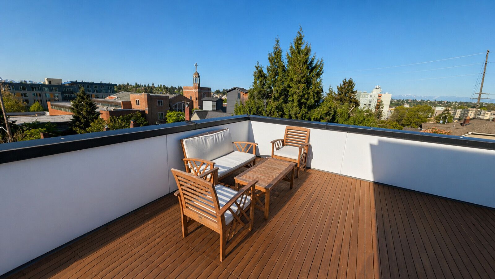 Eine Dachterrasse mit Holzmöbeln, blauem Himmel und Gebäuden im Hintergrund.