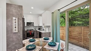 A modern kitchen with white cabinets, a stainless steel refrigerator, and a dining area with a glass table and teal plates. - 3BR 2.5BA Rooftop View Green Lake Hideaway near UW (Seattle)