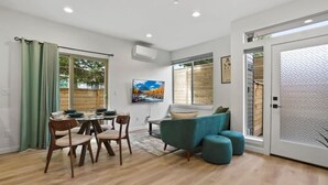 A modern living room with a dining area, featuring a large window, a painting, and a sliding glass door. - 3BR 2.5BA Rooftop View Green Lake Hideaway near UW (Seattle)