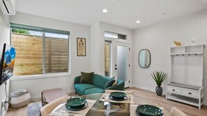 A modern living room with a glass dining table, teal sofa, and a piano. - 3BR 2.5BA Rooftop View Green Lake Hideaway near UW (Seattle)
