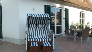 Un espace extérieur aménagé avec des sièges couverts, doté de coussins à rayures et de repose-pieds en bois, jouxtant une terrasse avec une table et des chaises.