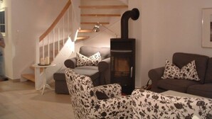 Un salon avec un escalier, une cheminée et deux canapés ornés de coussins à motifs.
