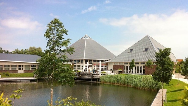 A building with a pond in front, surrounded by greenery and trees. - Beachvilla Grachtenblik (Makkum)
