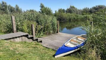 A small wooden dock leading to a calm river, with a blue boat tied to the dock.