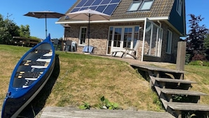A house with a sloped roof, solar panels, a covered patio, and a boat dock. - Beachvilla Grachtenblik (Makkum)
