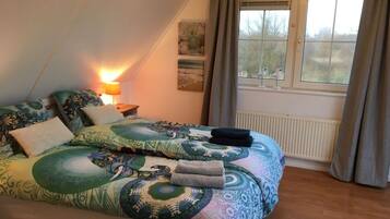 A bedroom with a bed, a nightstand, a lamp, a window with curtains, and a radiator.
