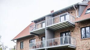 A multi-story brick building with a central courtyard, outdoor seating, and a pathway leading to the entrance. - Small House Lake Modern Retreat (Feldberger Seenlandschaft)