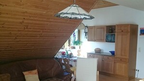 A cozy living room with a wooden ceiling, a dining table with a red placemat, and a white chair. - Daumler "house Am Weisswald" (Breitenbrunn/Erzgeb.)
