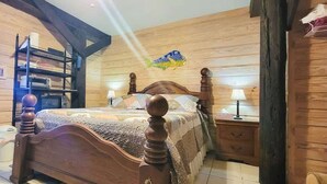 A wooden bedroom with a bed, a nightstand, a dresser, and a shelf with books and a lamp.