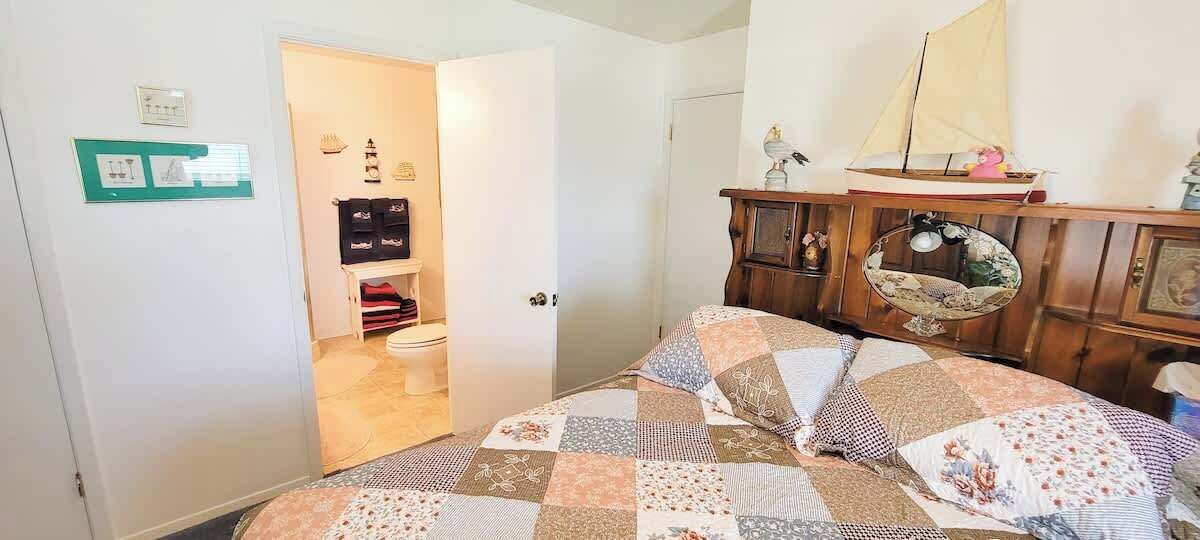 Un dormitorio con edredón acolchado, cómoda de madera y un pequeño modelo de velero encima.
